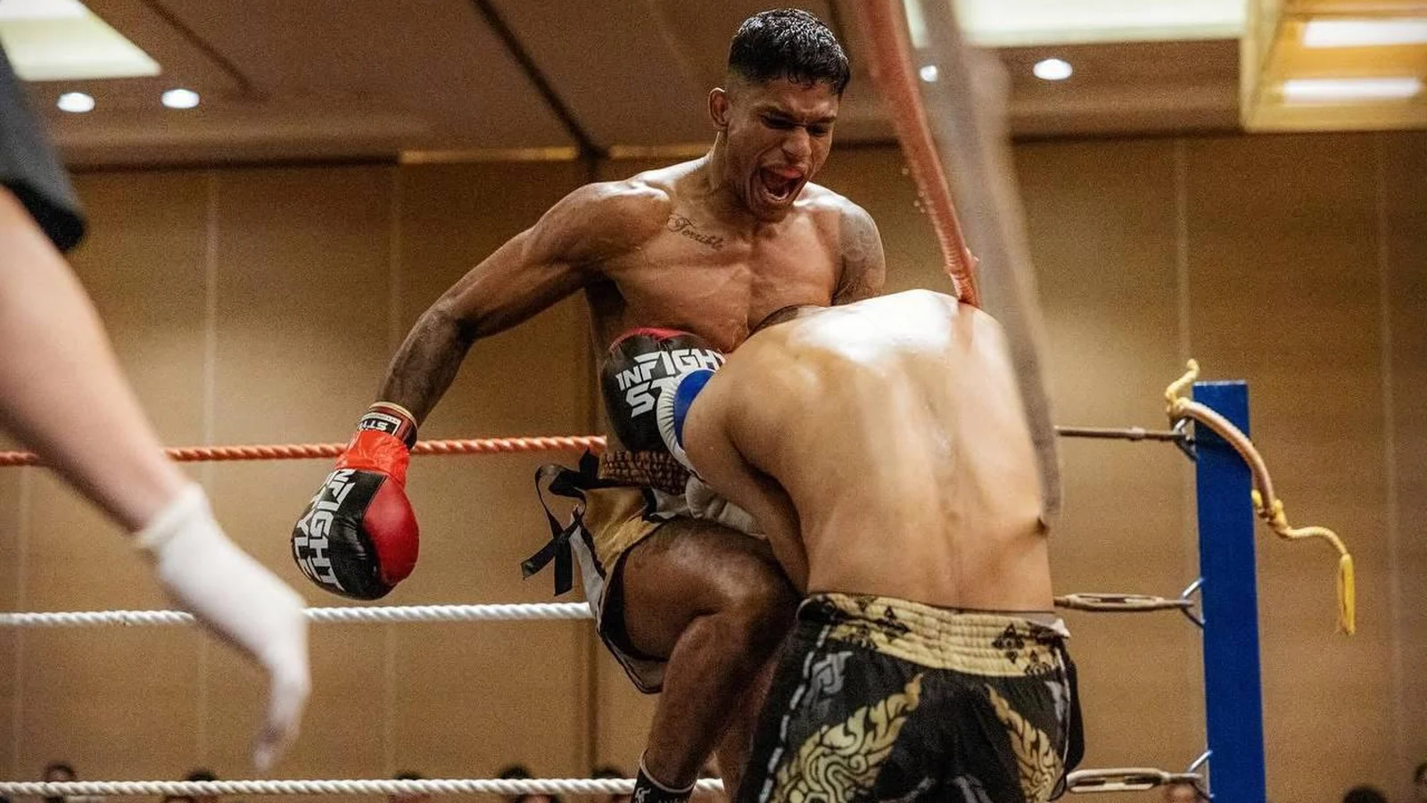 Sham Raaj driving a knee into his opponent in the corner of the ring, mid-fight